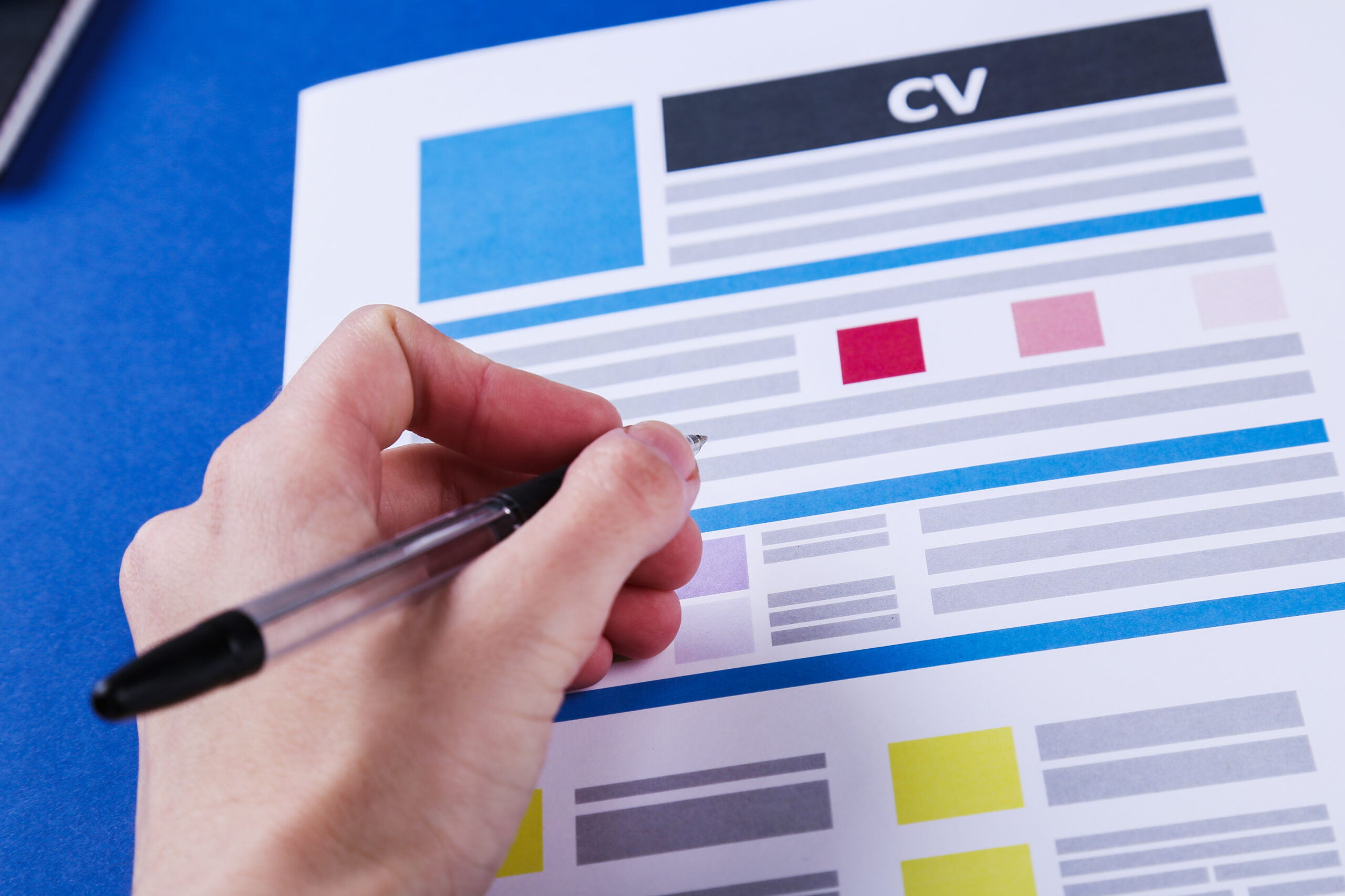 A candidate's hand with a pen writing a resume on a table.